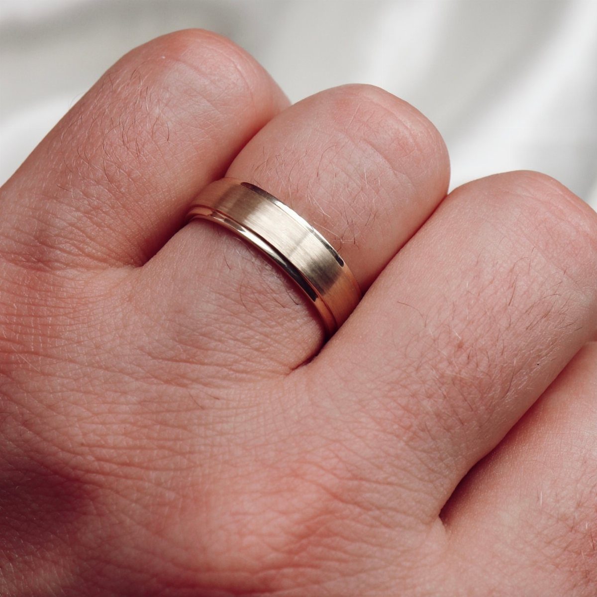 Gold wedding band with beveled edges worn on a person's ring finger.