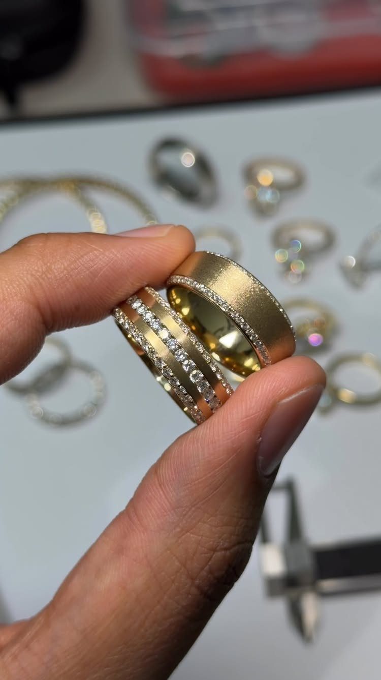 Two gold wedding bands with diamond accents held between a person's fingers.