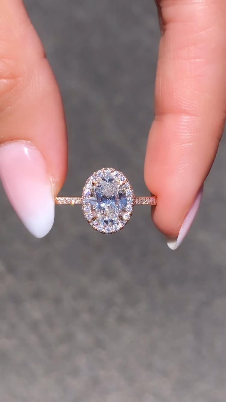 Rose gold halo engagement ring with oval center diamond held by two fingers.