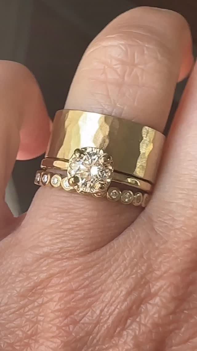 Three gold rings on a finger, including a hammered band and diamond rings.
