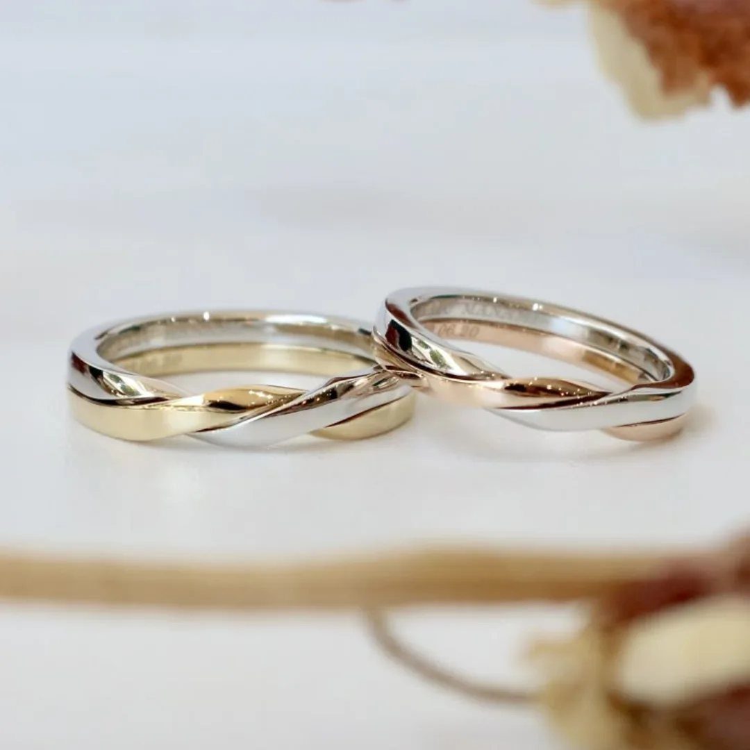 Two twisted wedding bands combining gold and silver metals on a white surface.
