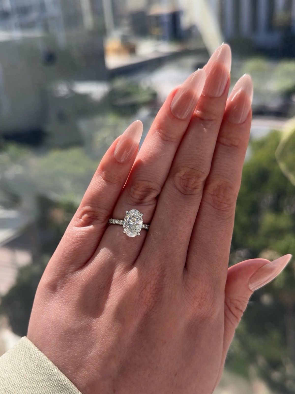Oval diamond engagement ring on a hand with long nude almond nails