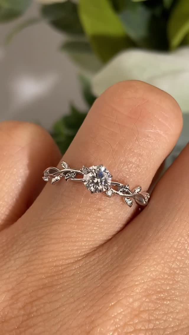Silver ring with leaf motifs and a central diamond on a finger