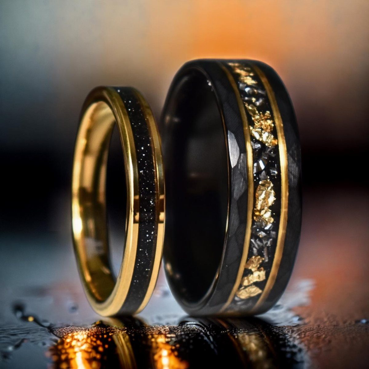 Two black and gold wedding bands with unique mineral inlays on reflective surface