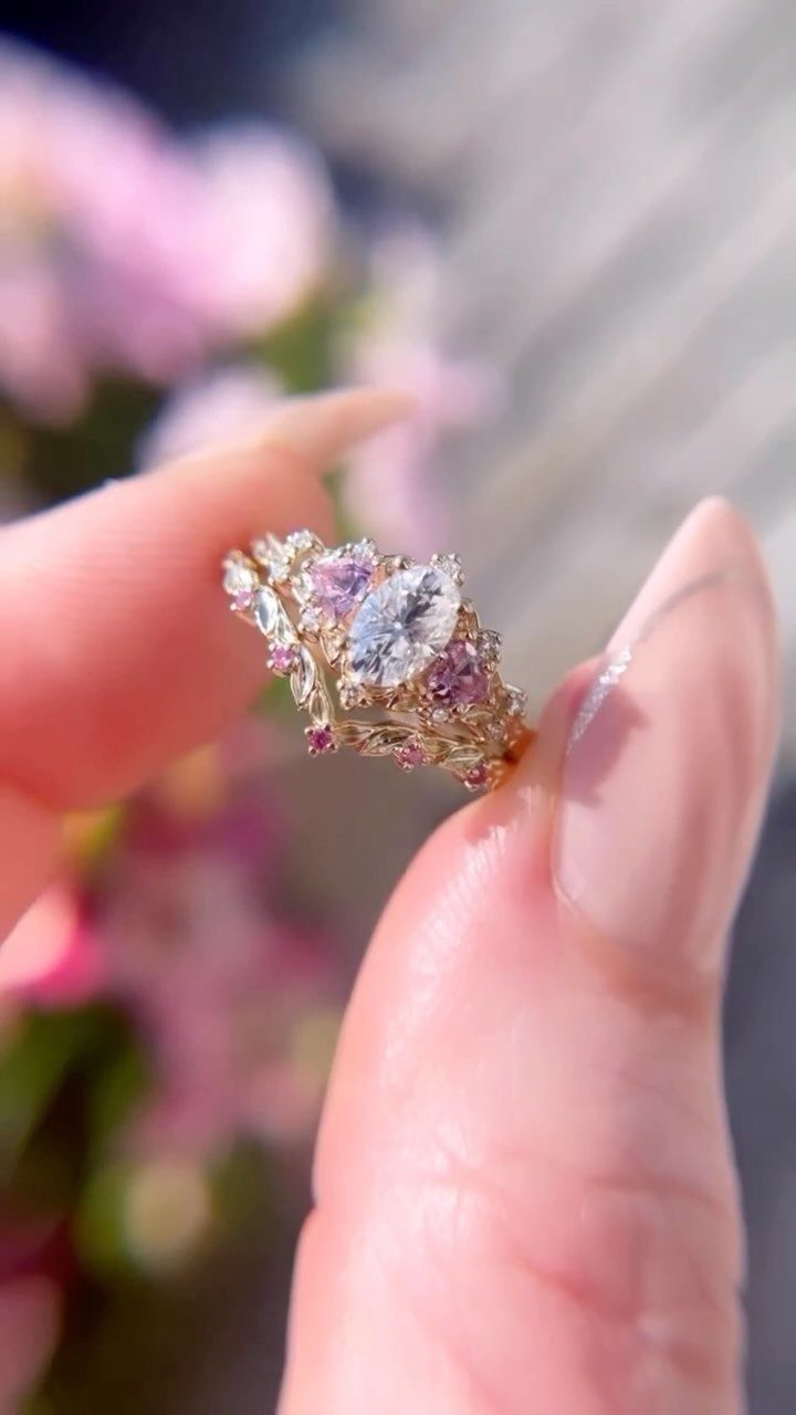 Gold ring with marquise diamond and pink gemstones held between two fingers.