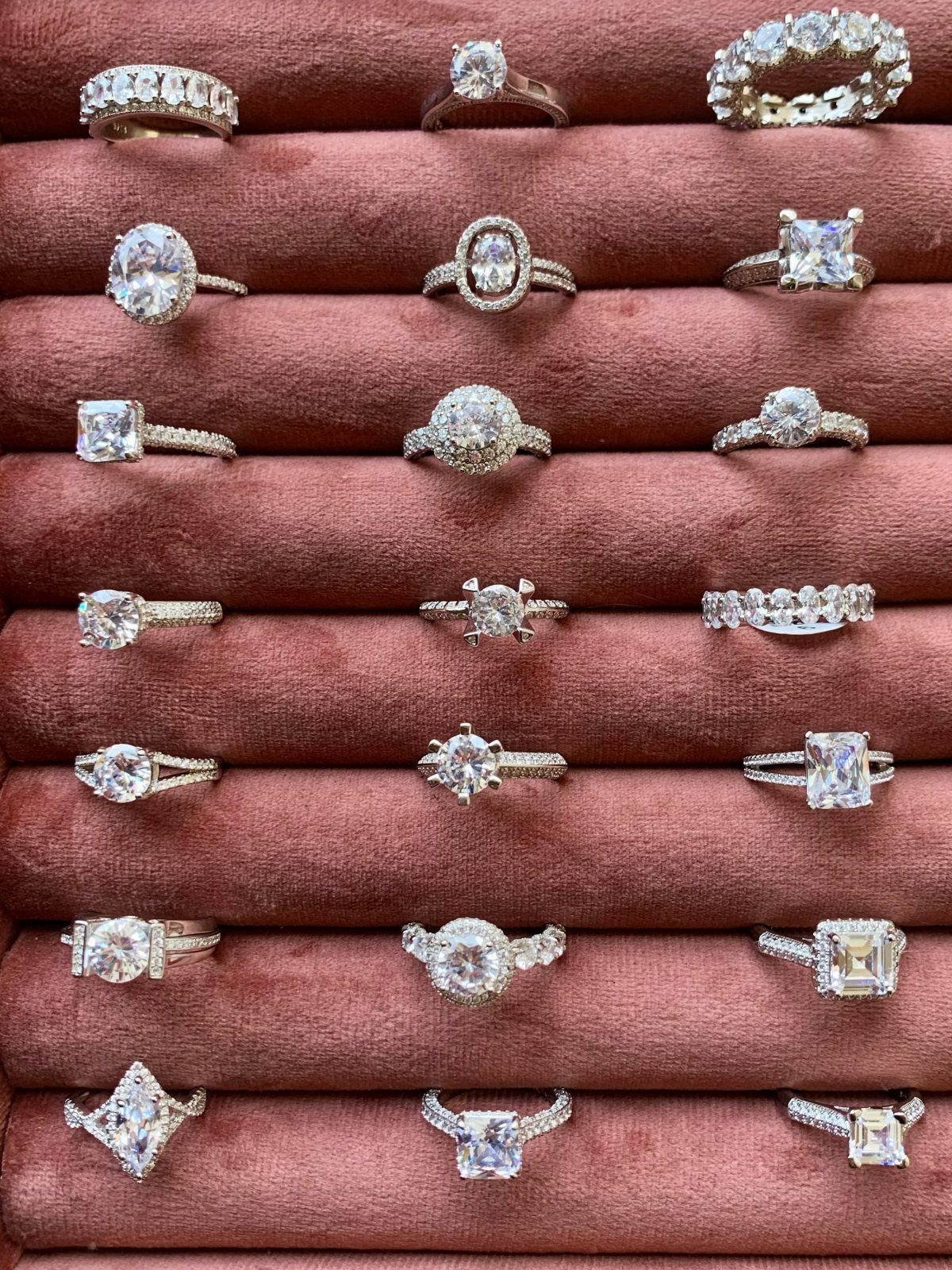 Various diamond rings displayed in a red velvet jewelry tray showing different styles.