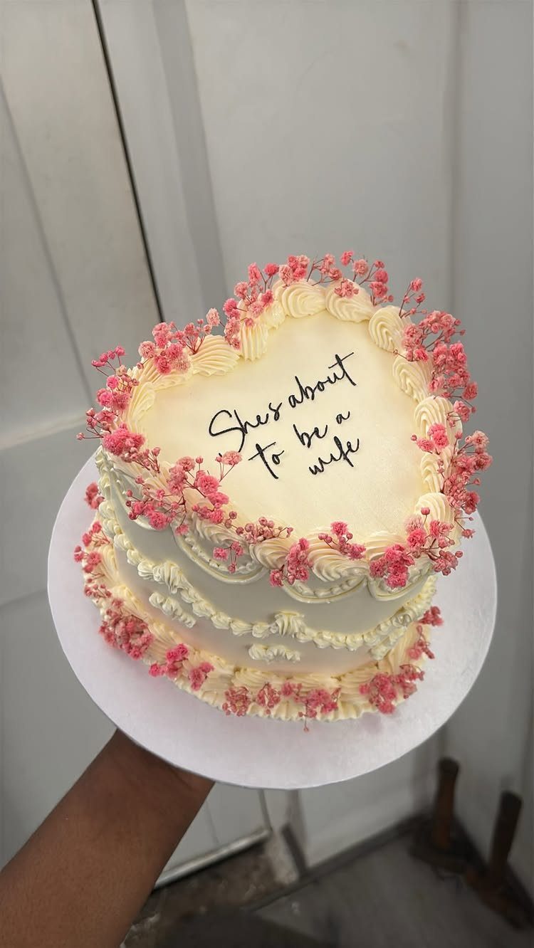 Heart-shaped white buttercream cake with pink flowers and bridal shower text.