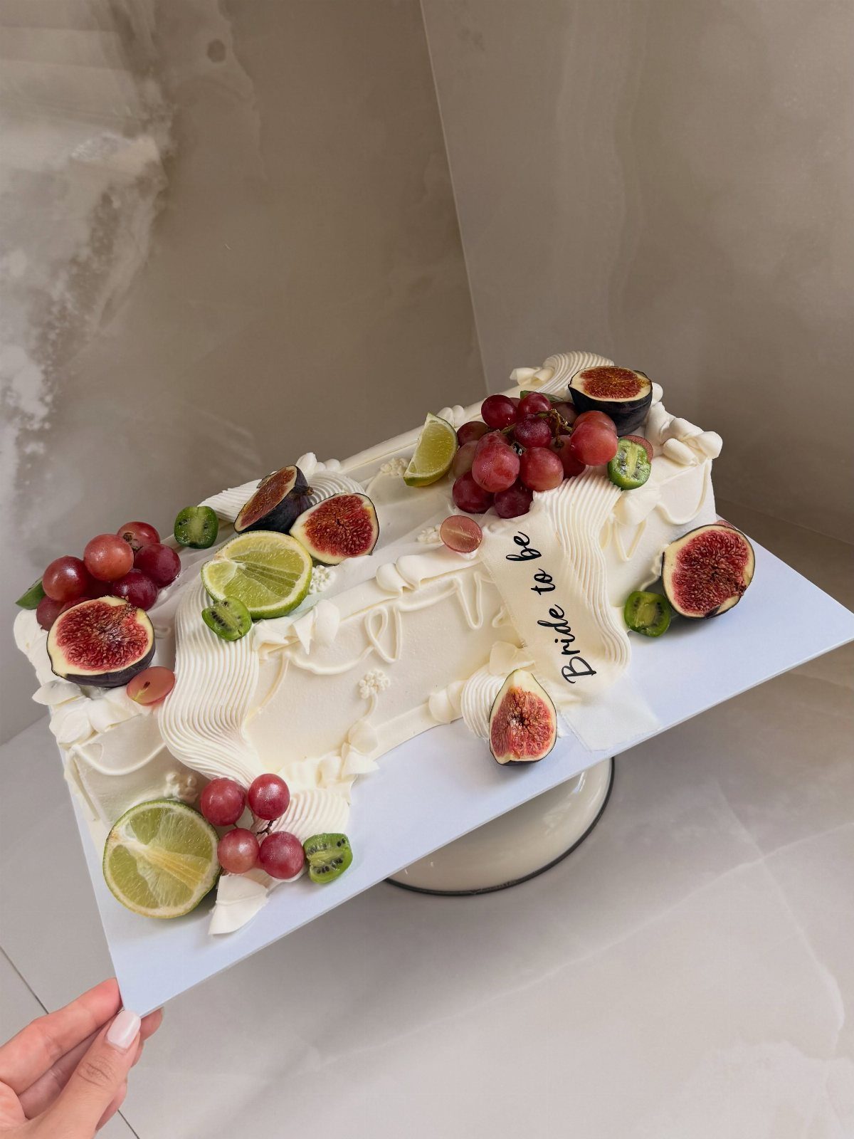 White frosted cake topped with fresh figs, grapes, and lime slices for a bride.