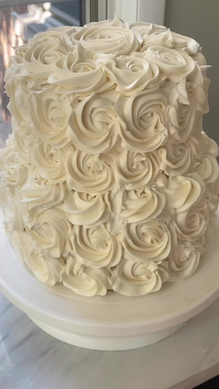 Two-tier white cake covered in buttercream icing rosettes on a white stand.