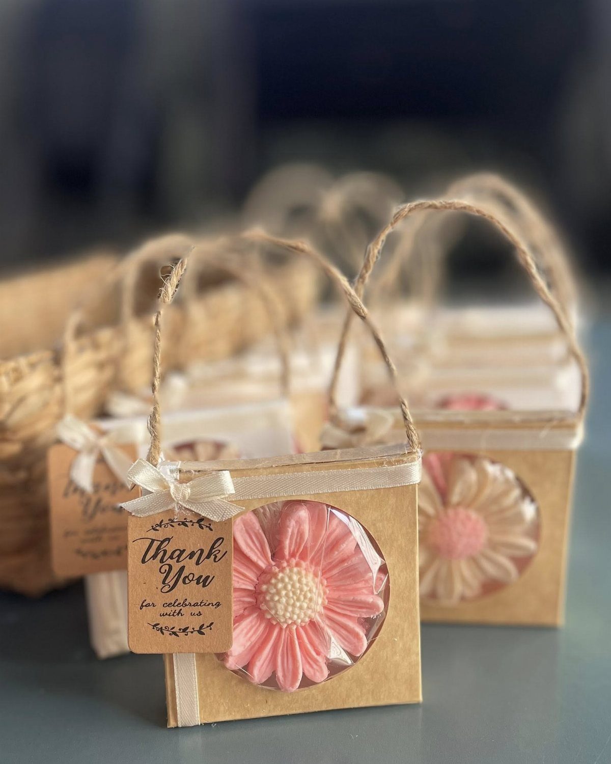 Pink flower-shaped soaps in small brown gift boxes with twine handles and tags.