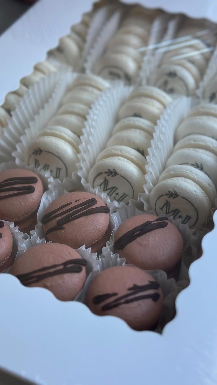 Macarons in a white box, some white with monograms and some brown with chocolate.
