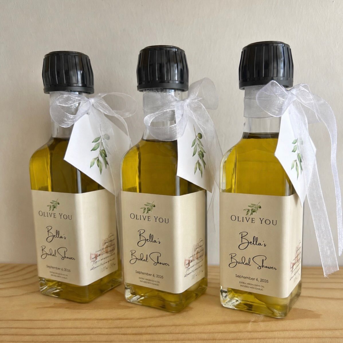 Three mini olive oil bottles with bridal shower labels and white ribbons.