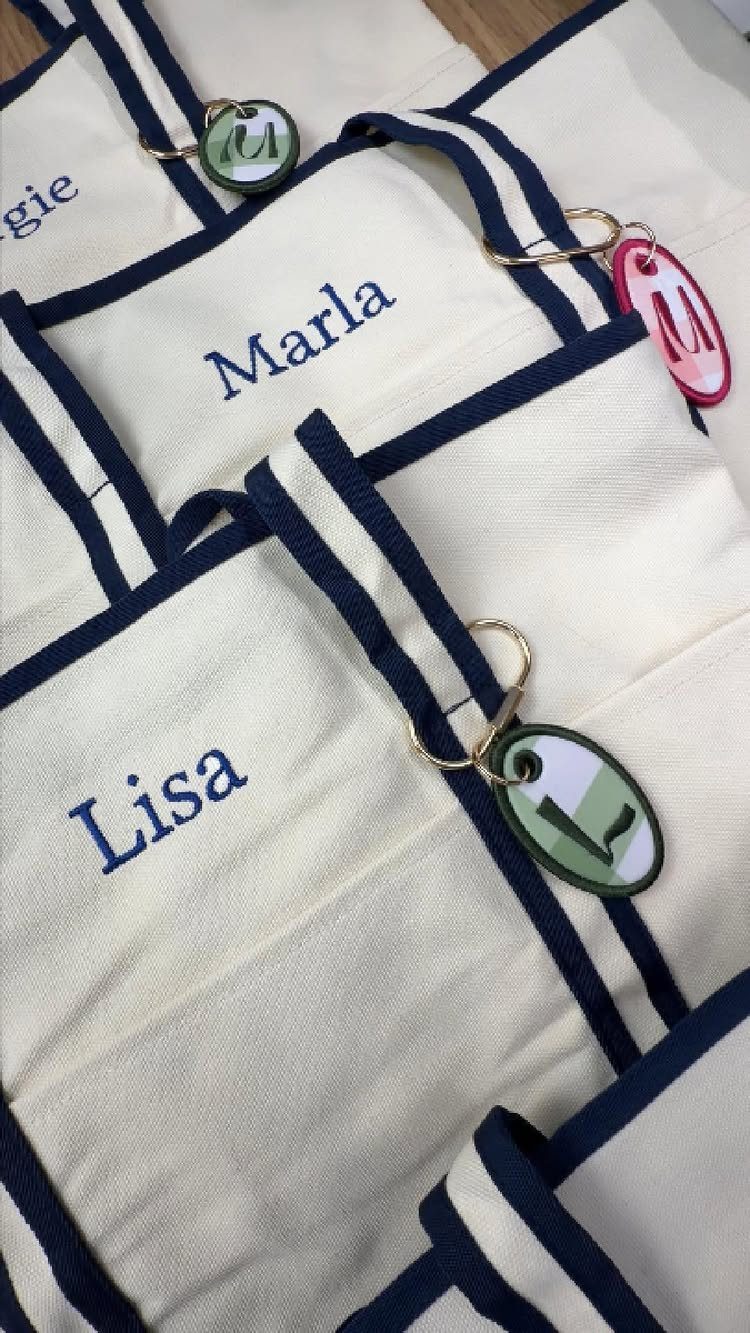 White embroidered bags with navy borders and custom oval letter keychains attached.
